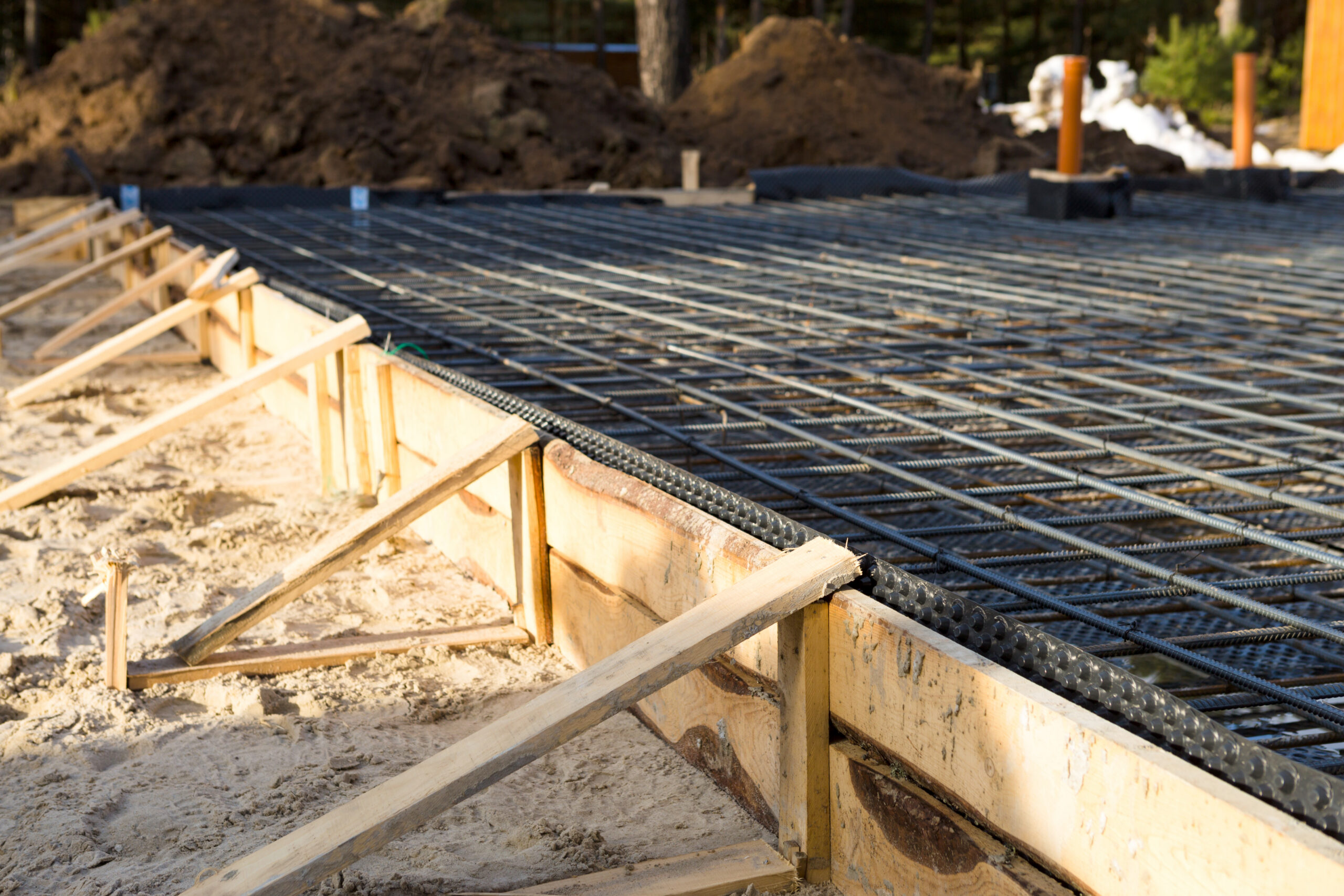 Steel reinforcement bars arranged in a grid pattern within a wooden formwork, prepared for pouring concrete to create a building foundation slab at a construction site.
