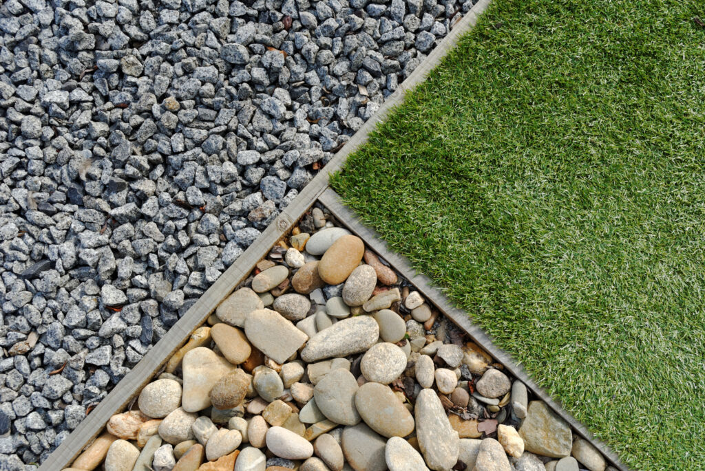 An overhead view of three garden sections: small gray gravel, smooth beige river rocks, and a patch of green grass, each separated by wooden borders.